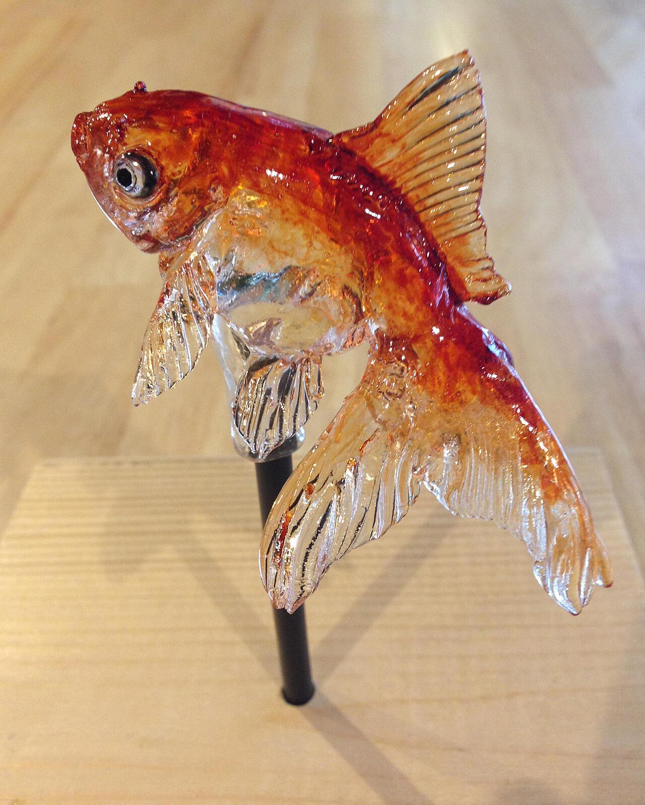 A translucent amezaiku goldfish sculpture displayed on a stick