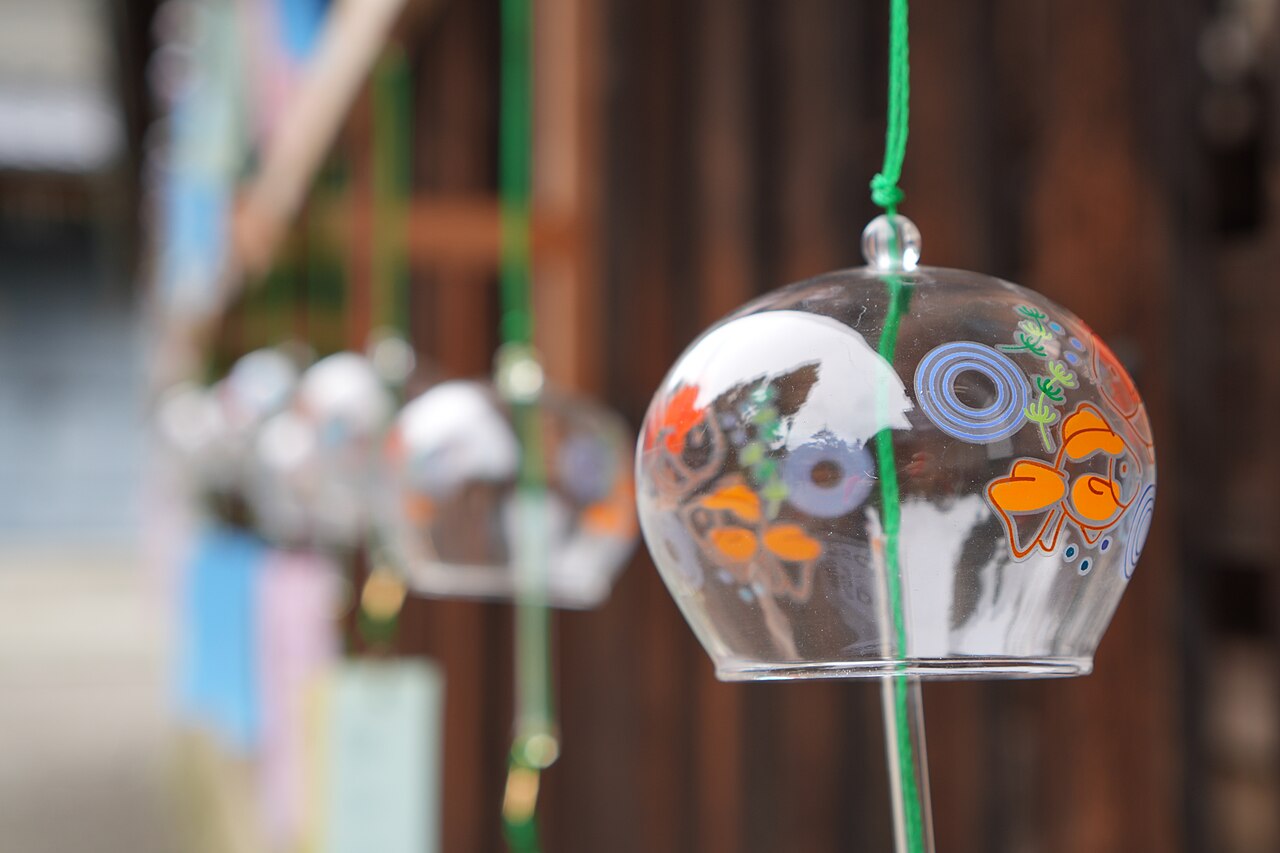 Close-up of a glass Edo furin wind chime painted with a goldfish design, hanging with other furin at a shrine