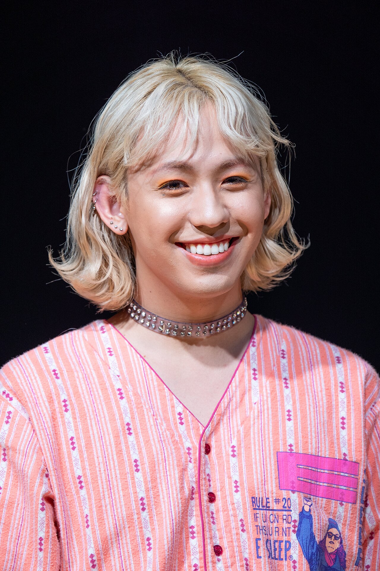 Ryuchell, one of the young Japanese TV personalities most associated with popularizing genderless kei, in dyed hair, soft eye makeup, and a choker at a 2019 talk event