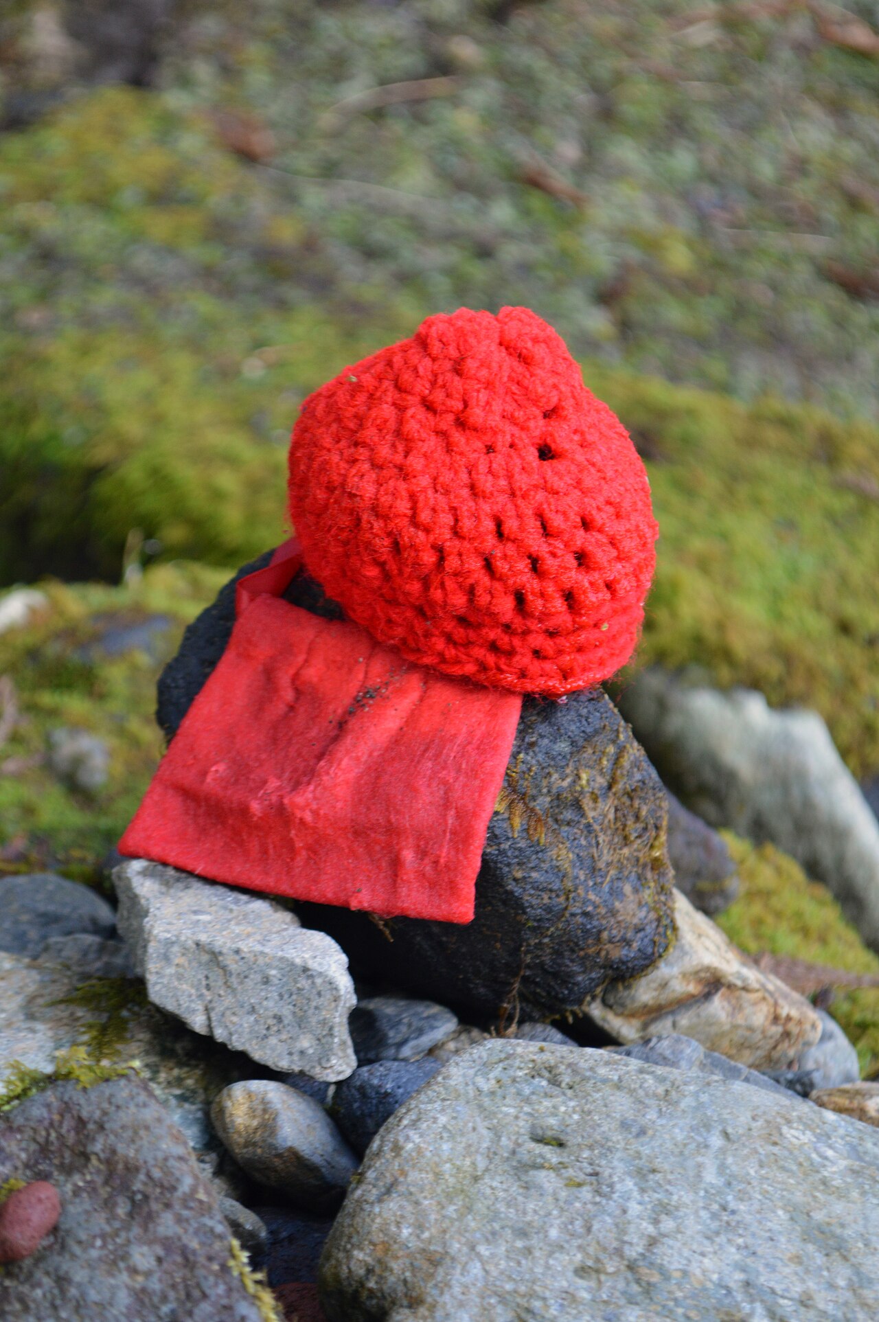 A small stone Jizō statue wearing a hand-knitted red cap and bib, at the Kanmangafuchi Abyss in Nikko