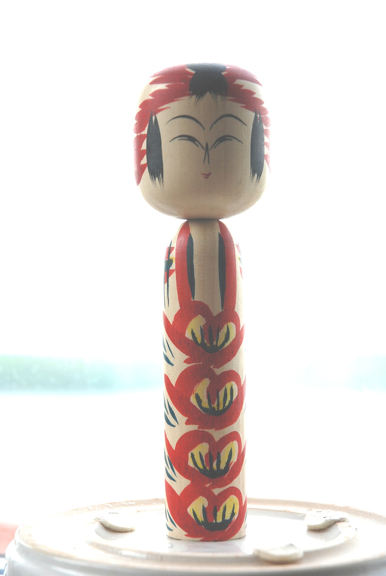 A traditional kokeshi doll with a painted floral robe and simple brushed face