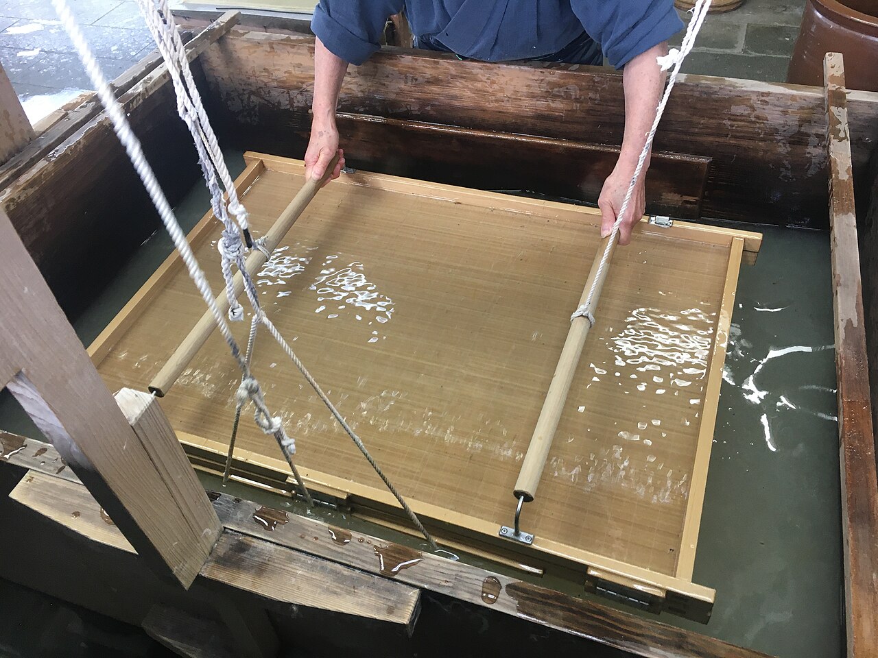 Craftsperson using the nagashizuki technique to form a sheet of washi in a vat of fiber suspension